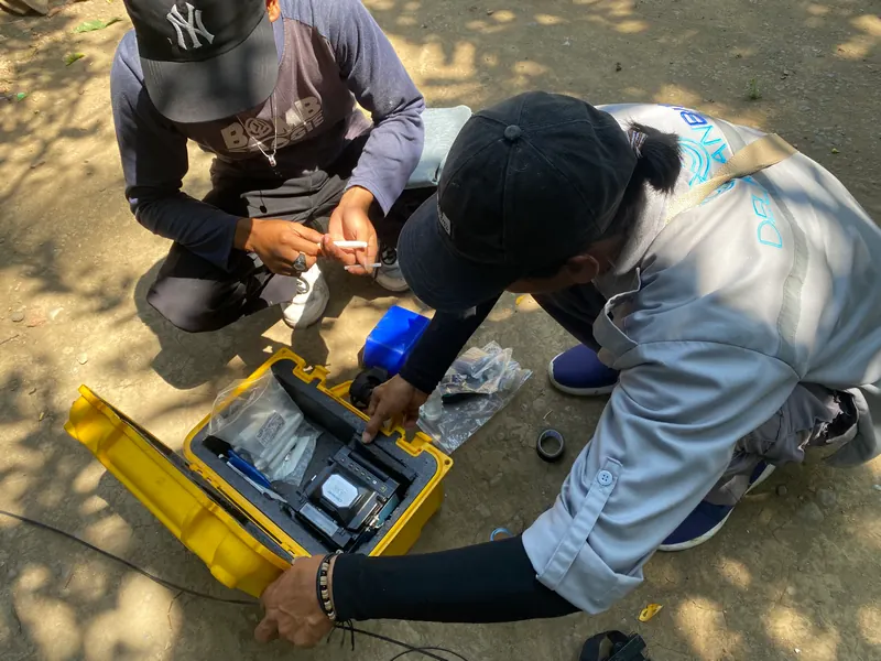 Teknisi melakukan splicing serat optik di pinggir jalan dengan pelindung terpal