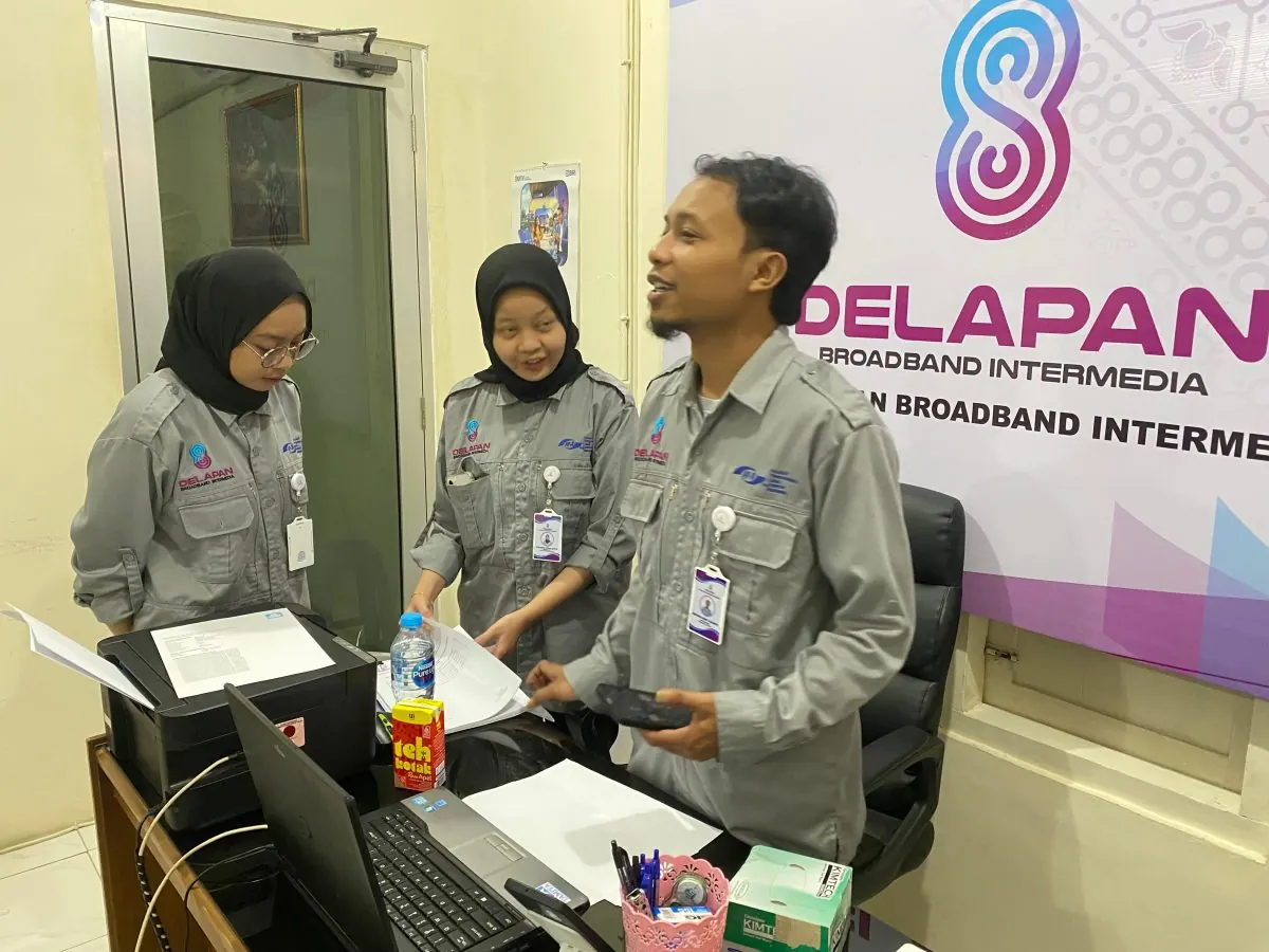 Staf kantor DelapanBit melakukan koordinasi dan diskusi dokumen di depan laptop